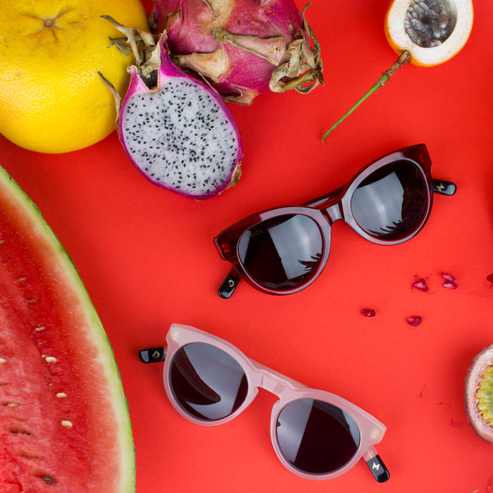 Two pairs of sunglasses next to some fruit.